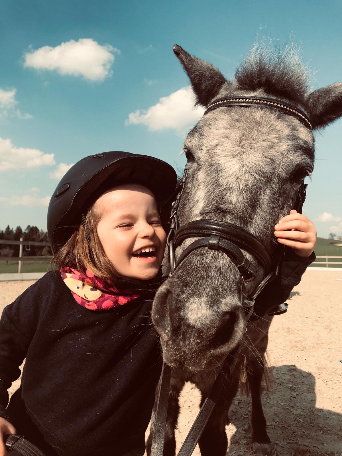  Kind mit Hut umarmt einen Pferdekopf - das Bild wird mit Klick vergrößert 